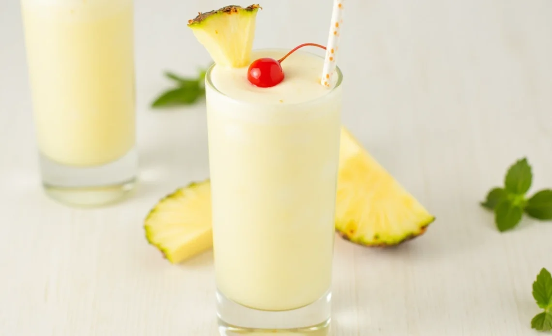 A refreshing virgin piña colada in a tall glass, garnished with a pineapple slice and cherry, with a tropical backdrop.