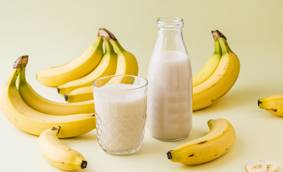 A bottle and glass of creamy Korean banana milk, served chilled with fresh bananas and a straw on the side.