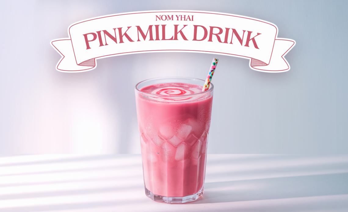 A glass of Nom Yen, a vibrant Thai pink milk drink, garnished with crushed ice and a straw, served in a colorful setting.