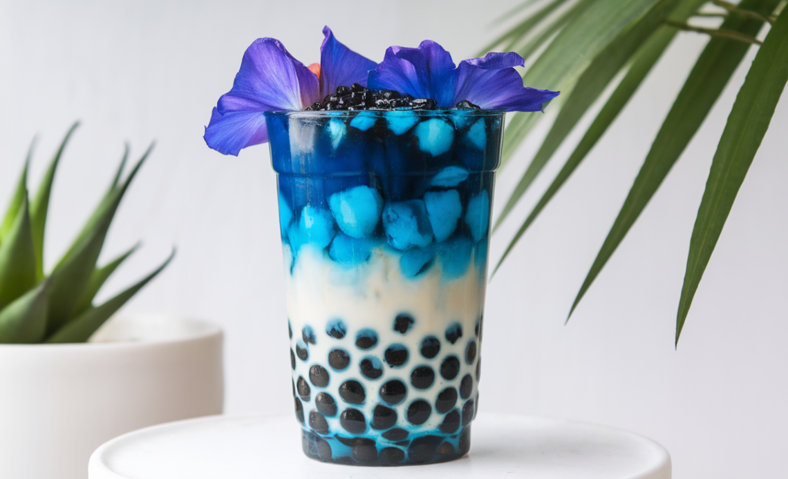 A refreshing glass of Coconut Butterfly Pea Flower Boba Tea with vibrant blue color, topped with boba pearls, and served with a straw.
